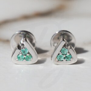May include: A pair of silver triangle stud earrings with three emerald green gemstones in each earring.