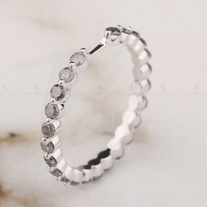 May include: A silver band ring with a row of small, round, gray diamonds.