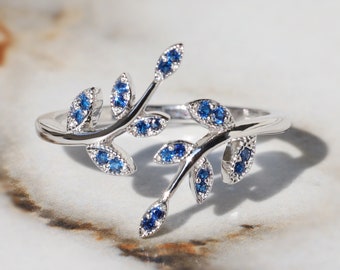 May include: A silver ring with a delicate branch design featuring blue gemstones. The ring is open and has a simple band.