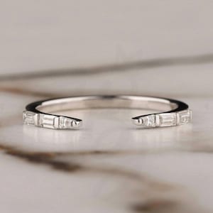 May include: A delicate silver ring featuring a row of small, rectangular-shaped diamonds set along the band. The ring is open on one side, creating a unique and modern design.