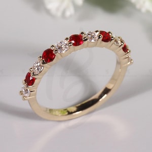 May include: A gold band ring featuring alternating red and clear gemstones. The ring's design showcases a series of vibrant red stones interspersed with sparkling clear stones, creating a classic and elegant look. The ring is a piece of jewelry.