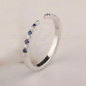 Op de afbeelding: Een delicate zilveren ring met een rij kleine blauwe en witte edelstenen. De ring is aan één kant open, waardoor hij verstelbaar is.
