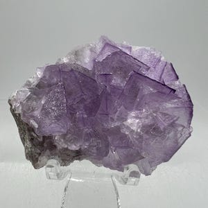 May include: A large purple fluorite crystal cluster with a variety of crystal shapes and sizes. The crystal is on a clear acrylic stand.