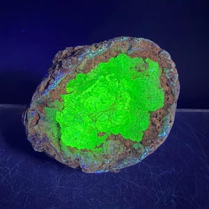 May include: A natural rock formation with a vibrant, neon green center. The rock has a rough, textured surface with shades of brown and hints of blue and green around the edges. The overall shape is irregular and organic.