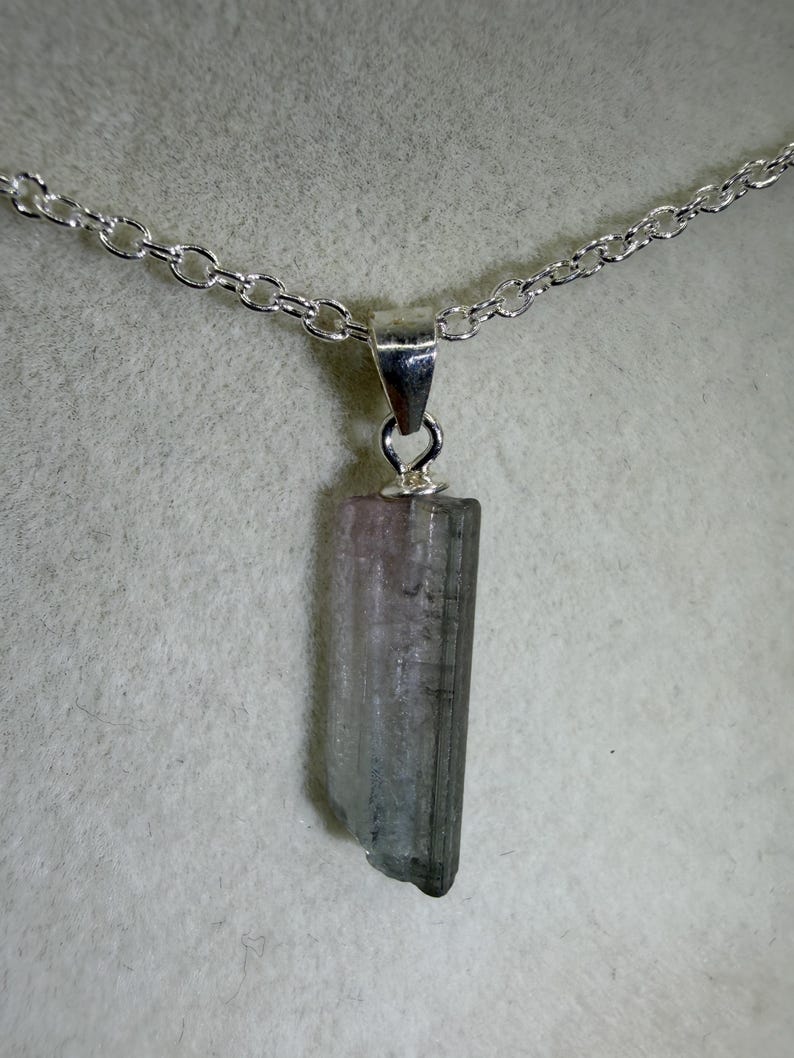 May include: A silver chain necklace featuring a rectangular tourmaline pendant. The pendant displays a blend of pink, grey, and clear hues. The tourmaline measures approximately 2.5 cm in length and is suspended from a fine silver chain.