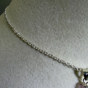 May include: A silver-toned metal chain necklace featuring a delicate link design. The chain is attached to a metallic bail that holds a vertical, translucent, pale pink rectangular gemstone pendant with a smooth, polished surface.
