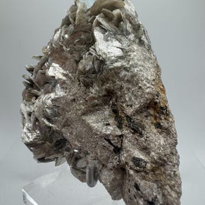 May include: A cluster of silvery-grey mica crystals with a light blue aquamarine crystal on top. The crystals are on a white background.