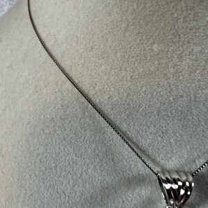 May include: A silver necklace with a rectangular pendant. The pendant features a mix of colors, including pink, white, and brown. The necklace chain is a dark silver color, and the pendant has a decorative silver bail.