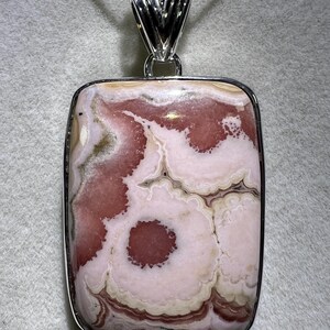 May include: A square pendant necklace featuring a polished stone with a unique pattern of pink, white, and beige swirls. The stone is set in a silver-colored metal frame and hangs from a delicate silver chain.