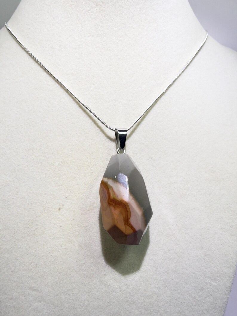 May include: A silver necklace featuring a faceted, teardrop-shaped pendant. The pendant showcases a blend of colors, including gray, brown, and white, with a polished finish. The necklace is displayed against a neutral background.