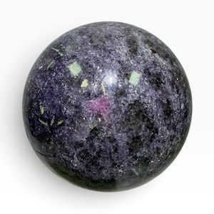 May include: A polished spherical stone featuring a deep purple and black mottled surface with a prominent, irregular bright pink inclusion near the center and small reflective crystalline flecks scattered throughout the textured mineral composition.