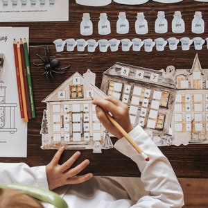 May include: A child is working on a math activity with two haunted house-themed game boards. The game boards have numbers and math symbols on them. The child is using a pencil to write on the boards. The game boards are on a wooden table.