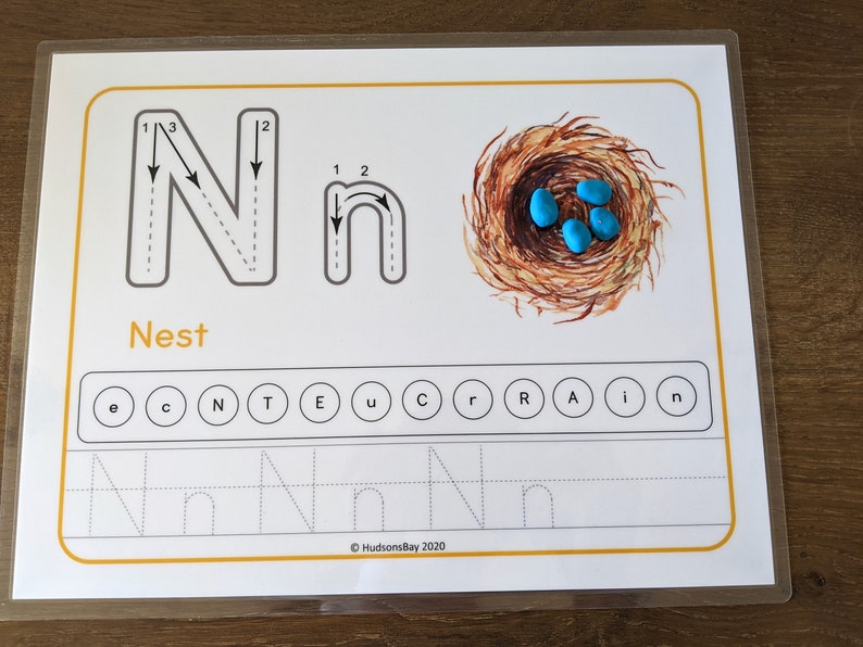 May include: A printable worksheet for learning the letter N. The worksheet includes a dotted line tracing guide for the uppercase and lowercase letter N, a picture of a nest with blue eggs, and a word search for the letter N. The text "Nest" is printed below the letter tracing guide. The text "HudsonsBay 2020" is printed in the bottom right corner of the worksheet.