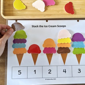 May include: A learning activity for kids featuring five ice cream cones with different colored scoops. The cones are arranged in a row and numbered 1 through 5. The text "Stack the Ice Cream Scoops" is at the top of the page.