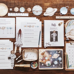 May include: A set of educational materials for children featuring a space theme. The set includes a variety of activities, such as a number chart, a counting game, and a worksheet. The materials are illustrated with planets, stars, and rockets.