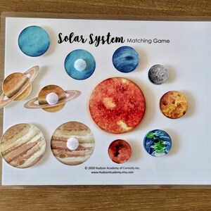 May include: A colorful solar system matching game with planets and a sun. The planets are illustrated with watercolor and have a white felt circle on the back for matching.