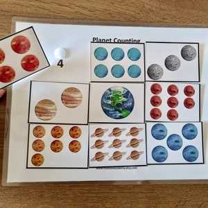May include: A printable educational game for kids featuring colorful planets with the title "Planet Counting". The game includes a set of cards with different planets and numbers to match.