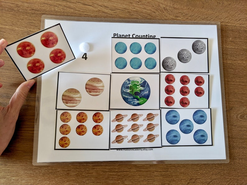 May include: A printable educational game for kids featuring colorful planets with the title "Planet Counting". The game includes a set of cards with different planets and numbers to match.