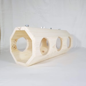 May include: A wooden hexagonal tube with three round holes cut into the side. The tube is made of unfinished wood and has a natural wood color.