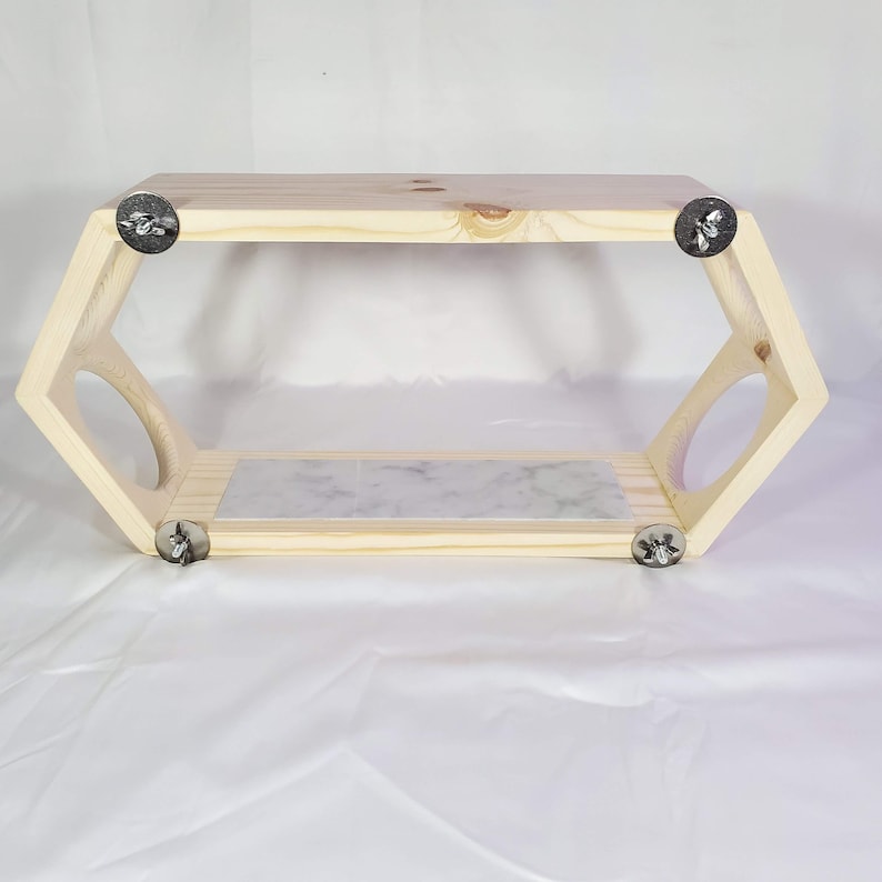 Puede incluir: Una estanter&iacute;a hexagonal de madera con una tapa de m&aacute;rmol y soportes de metal plateado. La estanter&iacute;a est&aacute; hecha de madera natural y tiene un aspecto r&uacute;stico.