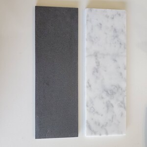 Puede incluir: Dos azulejos rectangulares, uno negro y otro blanco con vetas grises. Los azulejos est&aacute;n uno al lado del otro sobre una superficie blanca.
