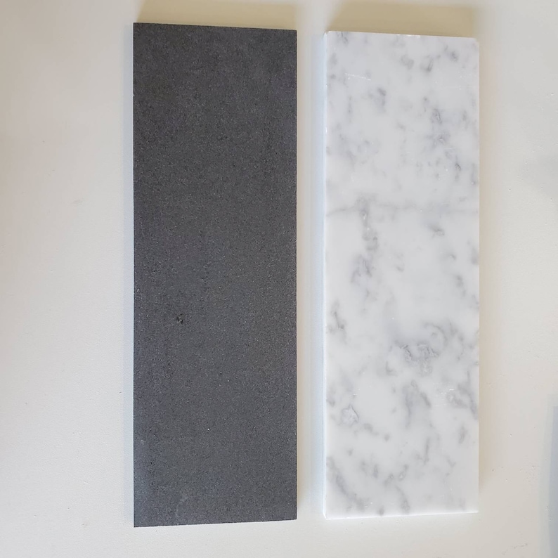 Puede incluir: Dos azulejos rectangulares, uno negro y otro blanco con vetas grises. Los azulejos est&aacute;n uno al lado del otro sobre una superficie blanca.