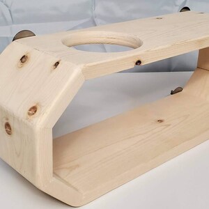 May include: A natural wood shelf with a rounded, hexagonal shape. The shelf has a cutout for a cup or mug and is designed to be mounted on a wall.