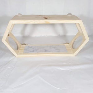 Puede incluir: Una estanter&iacute;a hexagonal de madera con una tapa de m&aacute;rmol. La estanter&iacute;a tiene dos c&iacute;rculos recortados en los lados y est&aacute; fijada a la pared con adhesivo transparente.