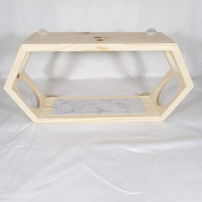 Puede incluir: Una estanter&iacute;a hexagonal de madera con una tapa de m&aacute;rmol. La estanter&iacute;a tiene dos c&iacute;rculos recortados en los lados y est&aacute; fijada a la pared con adhesivo transparente.