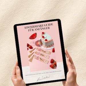 Könnte beinhalten: Ein Tablet zeigt einen Ratgeber mit dem Titel "EPOXIDHARZ GUIDE FÜR ANFÄNGER" auf rosa Hintergrund. Das Bild zeigt einen herzförmigen Kuchen, Erdbeeren, ein Glas rote Flüssigkeit und dekorative Lesezeichen. Der Text lautet "DER EINFACHE EINSTIEG IN DIE WELT DER RESIN-KUNST".