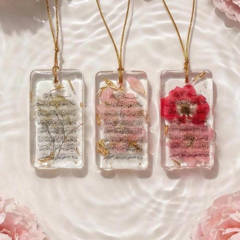 May include: Three rectangular resin pendants with gold chains. Each pendant features dried flowers and script. One pendant has a red flower, another has pink flowers, and the third has dried greenery.