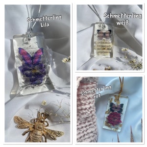 May include: Three rectangular resin pendants with butterfly and floral designs. One pendant features a purple butterfly and text, another a white butterfly, and the third a red butterfly. Each pendant is on a silver or gold chain.