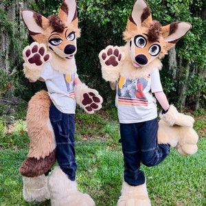 May include: Two furry animal costumes, one brown and tan, the other brown and white, with large ears and paws. Both costumes are wearing jeans and a white t-shirt. The costumes are standing in a grassy area.