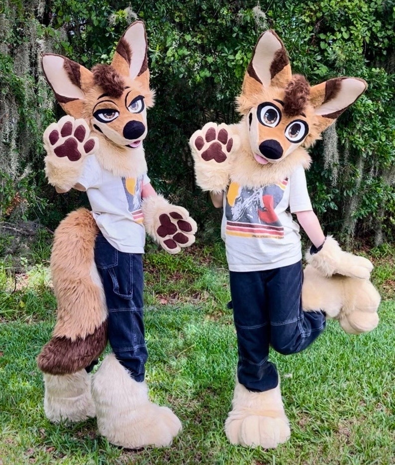 May include: Two furry animal costumes, one brown and tan, the other brown and white, with large ears and paws. Both costumes are wearing jeans and a white t-shirt. The costumes are standing in a grassy area.