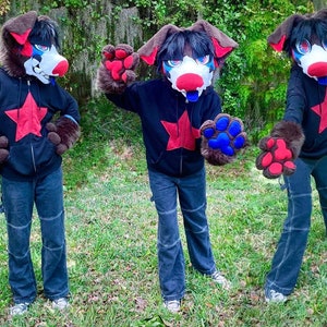 May include: Three furry dog costumes with black hoodies featuring a red star. The costumes have brown fur, red and blue paw-shaped hands, and black and white masks.