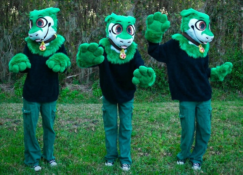 May include: Three green fursuit heads with black sweaters and green pants. The fursuits have green fur and white faces with black eyes and pink noses.