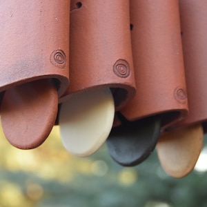 May include: A set of terracotta wind chimes with a white, black, and brown clapper. The chimes are decorated with a swirl design.