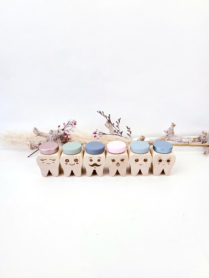 May include: Six wooden teeth with different facial expressions and colored tops. The teeth are arranged in a row on a white surface.