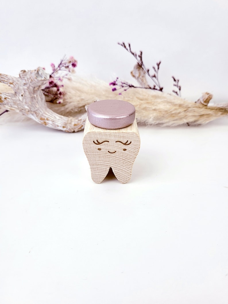May include: A wooden tooth with a pink glitter top. The tooth has a smiling face with eyelashes.