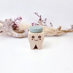 May include: A wooden tooth with a smiling face and large eyes. The tooth is holding a light blue round object on top.