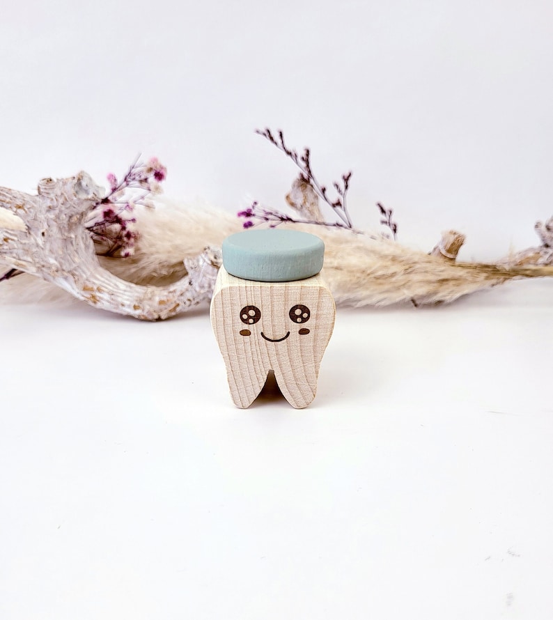 May include: A wooden tooth with a smiling face and large eyes. The tooth is holding a light blue round object on top.