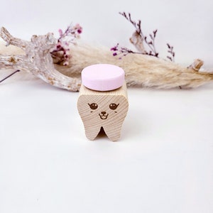 May include: A wooden tooth with a cute cartoon face, holding a pink chewable tablet.