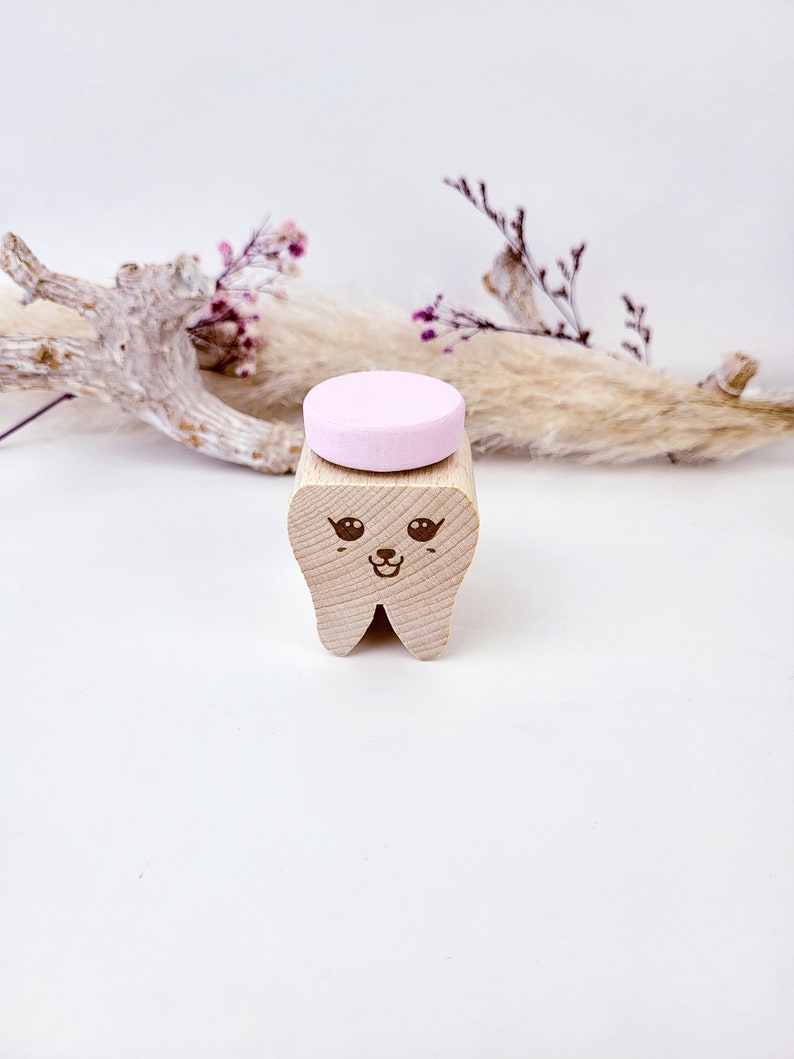 May include: A wooden tooth with a cute cartoon face, holding a pink chewable tablet.
