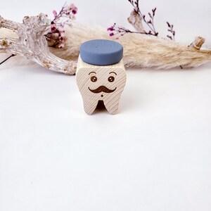 May include: A wooden tooth with a painted face, a mustache, and a blue hat. The tooth is a decorative object.