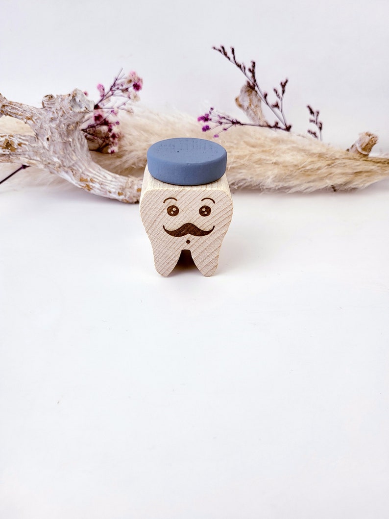May include: A wooden tooth with a painted face, a mustache, and a blue hat. The tooth is a decorative object.