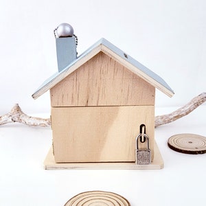 Peut inclure: Une tirelire en bois en forme de maison avec un toit bleu clair et un bouton argent&eacute; sur le dessus. La tirelire a une serrure sur le c&ocirc;t&eacute;.
