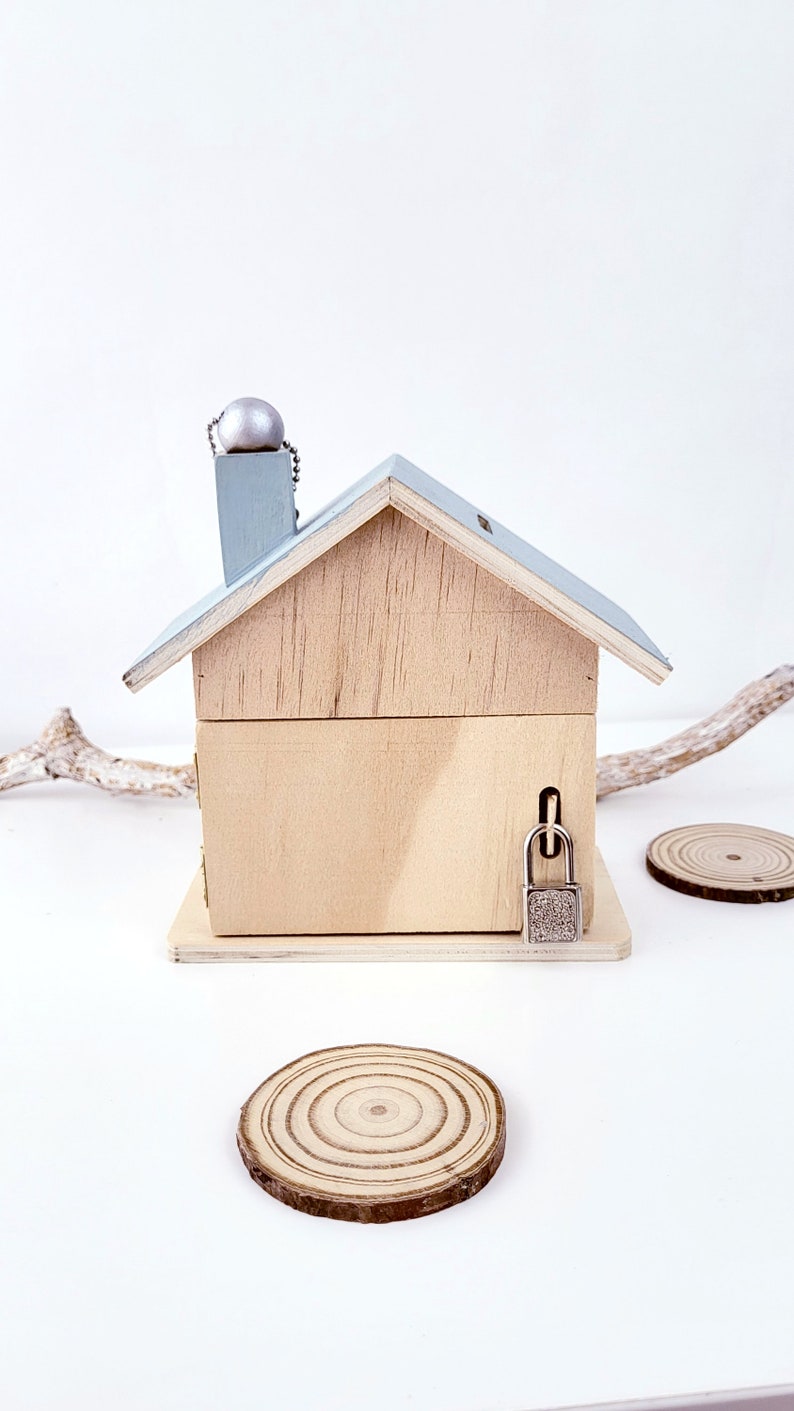 Peut inclure: Une tirelire en bois en forme de maison avec un toit bleu clair et un bouton argent&eacute; sur le dessus. La tirelire a une serrure sur le c&ocirc;t&eacute;.