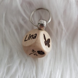 May include: Wooden keychain with a butterfly and rose design. The keychain is engraved with the name "Lina".