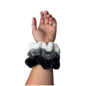 May include: A set of three scrunchies in black, gray, and white. The scrunchies are made of a soft, fluffy material.