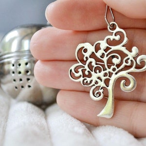 May include: A silver tree-shaped pendant with intricate details. The pendant is held in a hand with a ring on the finger.
